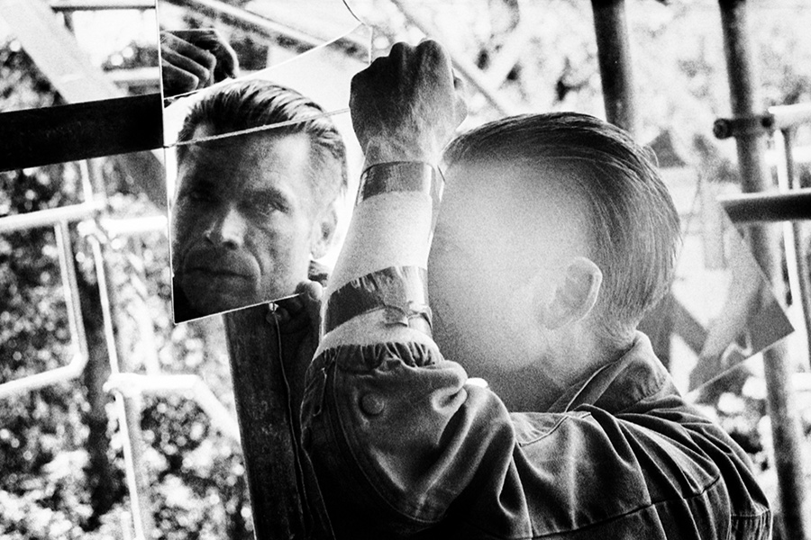 Zenith analog, inszeniertes Schwarzweißfoto, Mann hält zwei Spiegelstücke mit Gesichtsreflexion, hartes Gegenlicht, gepushter Film, Doppelporträt