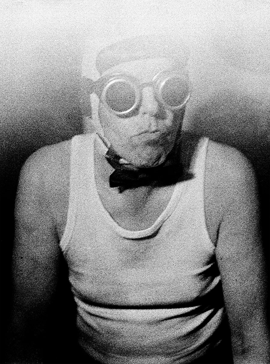Schwarzweißfotografie analog Mittelformat: Mann mit Schweißerbrille und Vampirzähnen, Kopf leicht gesenkt, ruhige Haltung, weiches Graukorn, Mamiya, Antje Kröger