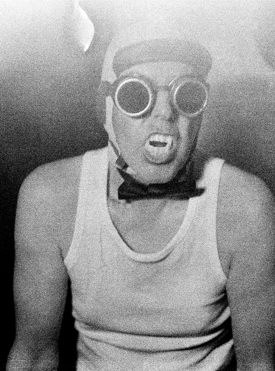 Analoges Schwarzweißporträt auf Mittelformat: Mann mit Schweißerbrille und Vampirzähnen im Unterhemd mit Fliege, Mamiya Mittelformatfilm, Fotografie Antje Kröger