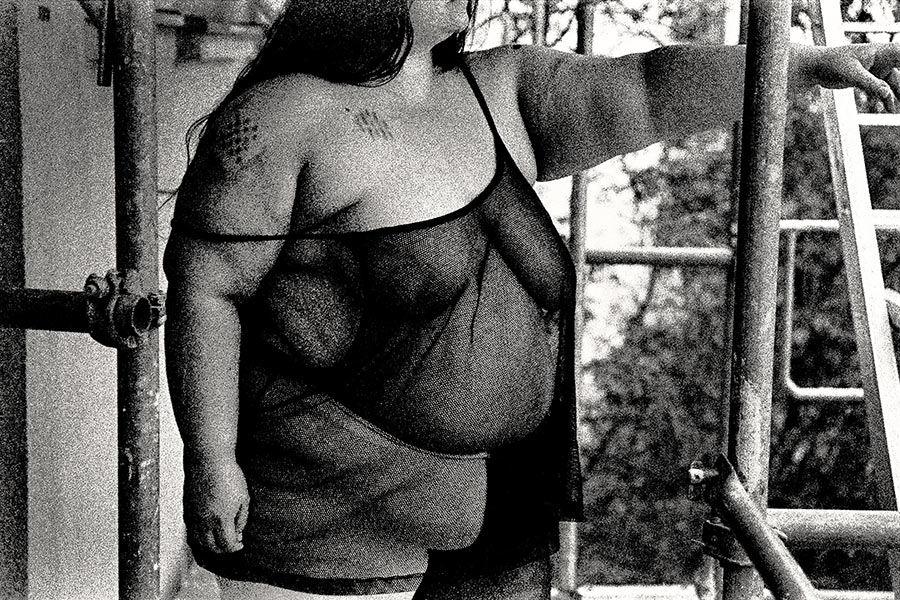 Körpermitte ohne Gesicht, Tattoos auf Schulter, stehend auf Gerüst, körniges 35mm-Schwarzweiß – analoge Körperfotografie Antje Kröger Leipzig Berlin, Serie Walsturz