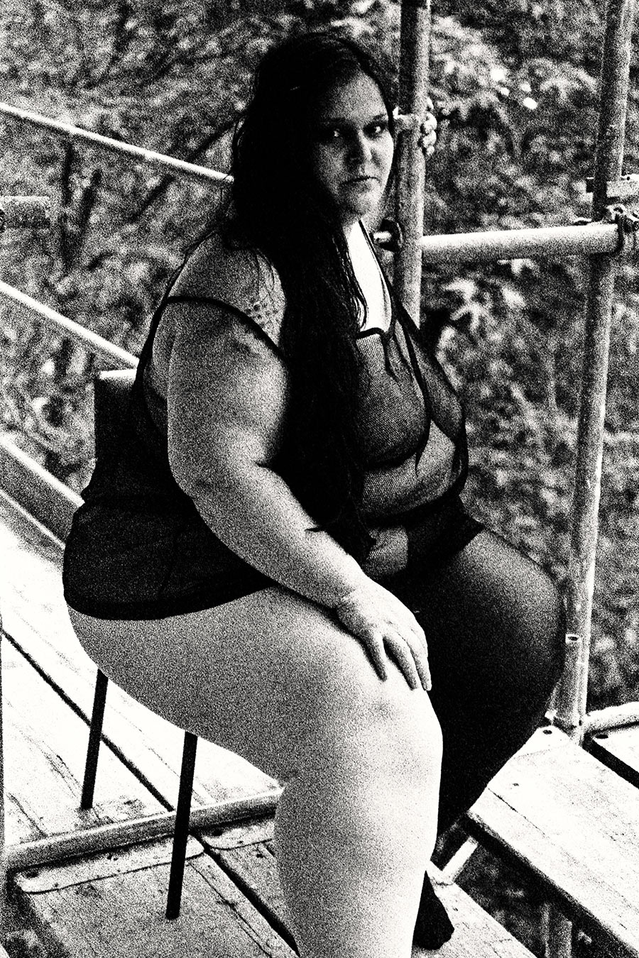 Frau sitzt auf Stuhl auf Gerüst, Blick zur Seite, bekleidet, Sommerlaub, nachdenkliche Haltung, analoges Schwarzweiß-Porträt – Antje Kröger Fotografie Leipzig, Serie Walsturz