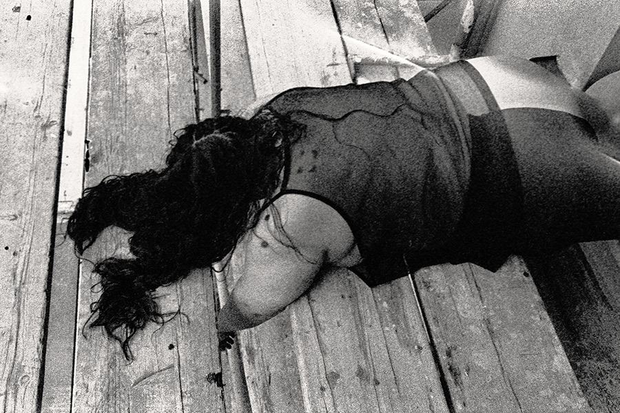 Frau liegt auf verwitterten Holzdielen des Gerüsts, Gesicht im Haar verborgen, von oben fotografiert, 35mm-Kleinbild-Schwarzweiß – Antje Kröger Körperfotografie Leipzig, Serie Walsturz