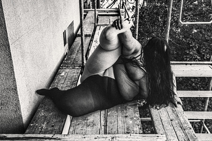 Dicke Frau auf Gerüst liegend, Beine hochgezogen, Hände an Gerüststange, Haar ausgebreitet, Herbst, 35mm-Analogfoto – Antje Kröger Fotokunst Leipzig, Serie Walsturz