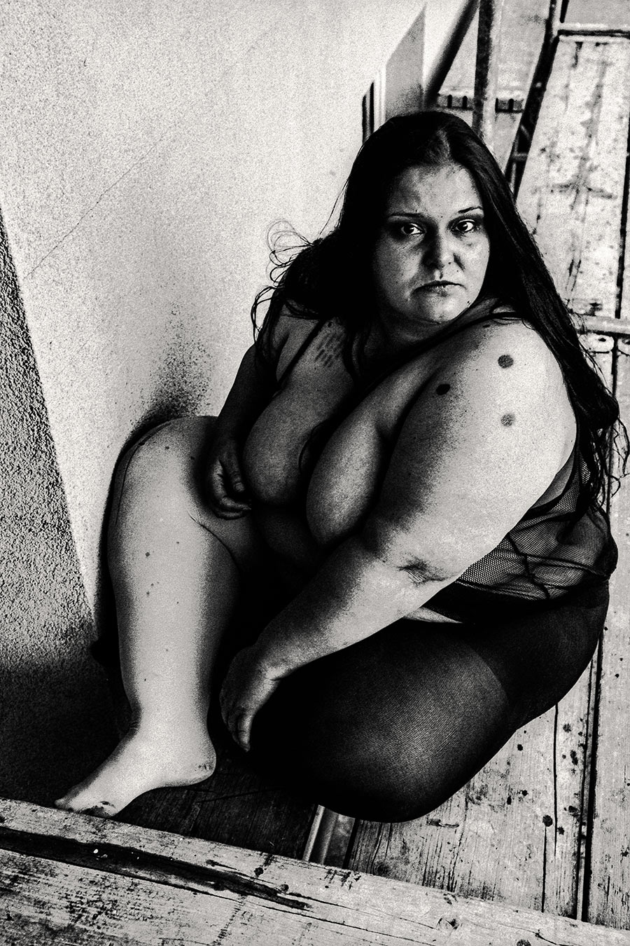 Direkter Blick in die Kamera, Frau zusammengekauert auf Gerüst, starkes 35mm-Korn, Körper kompakt und präsent – Fotokunst Antje Kröger Leipzig, Serie Walsturz
