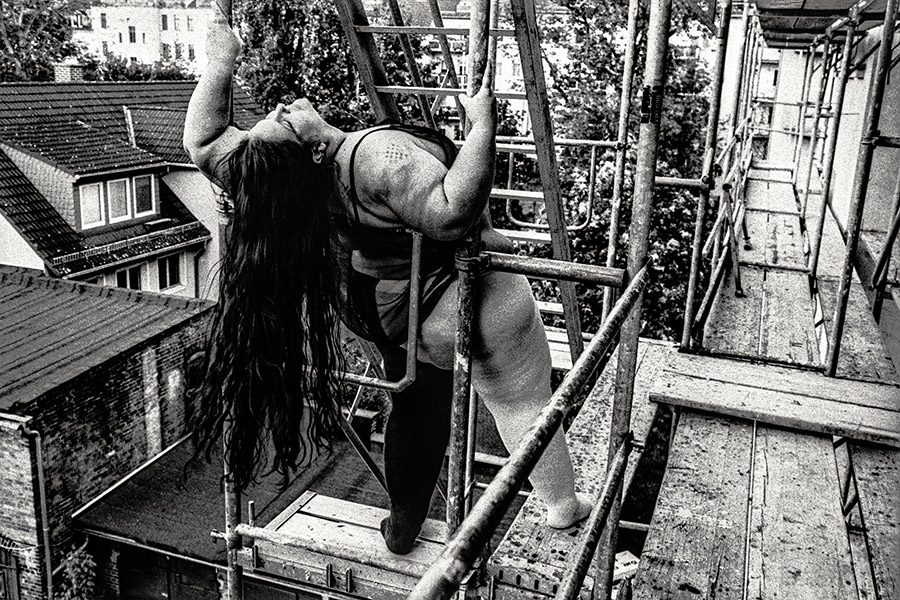Dicker Körper steigt Metallleiter hoch, Bauch und Schenkel prominent, Aufnahme von unten, Sommerlaub, 35mm-Kleinbild – Körperfotografie Antje Kröger Leipzig, Serie Walsturz