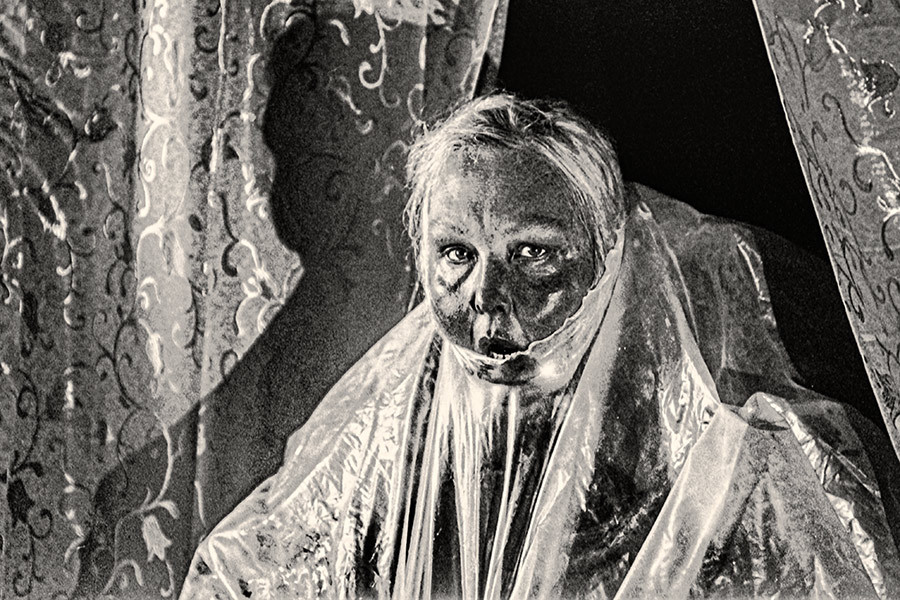 Schwarzweißfoto einer Frau, deren Gesicht eng von transparenter Folie umhüllt ist, analoges Körnungsbild auf Fomapan Ortho 400