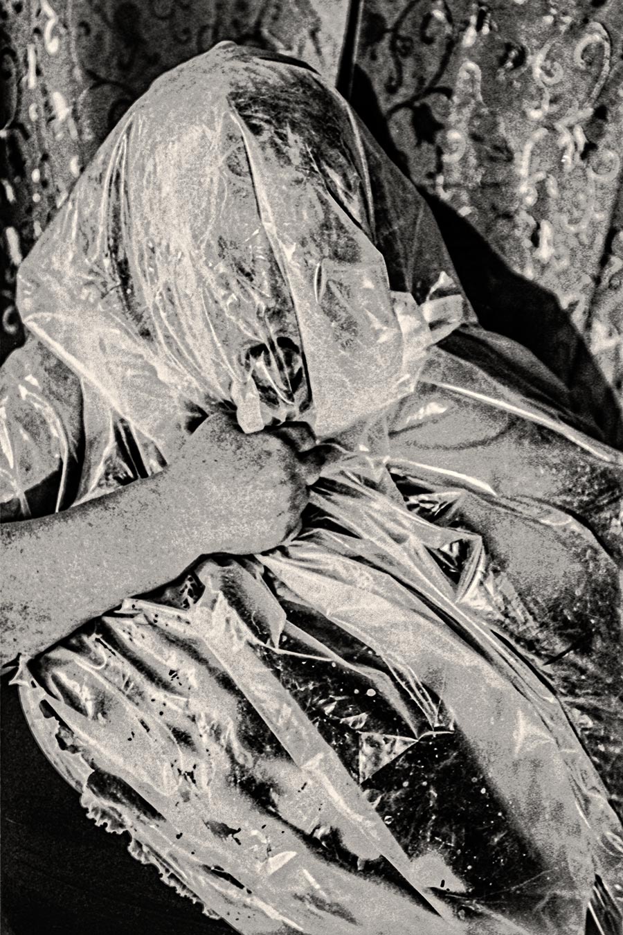 Nahaufnahme einer Hand die transparente Folie über ein Gesicht zieht, analoges Schwarzweißfoto auf Fomapan Ortho 400