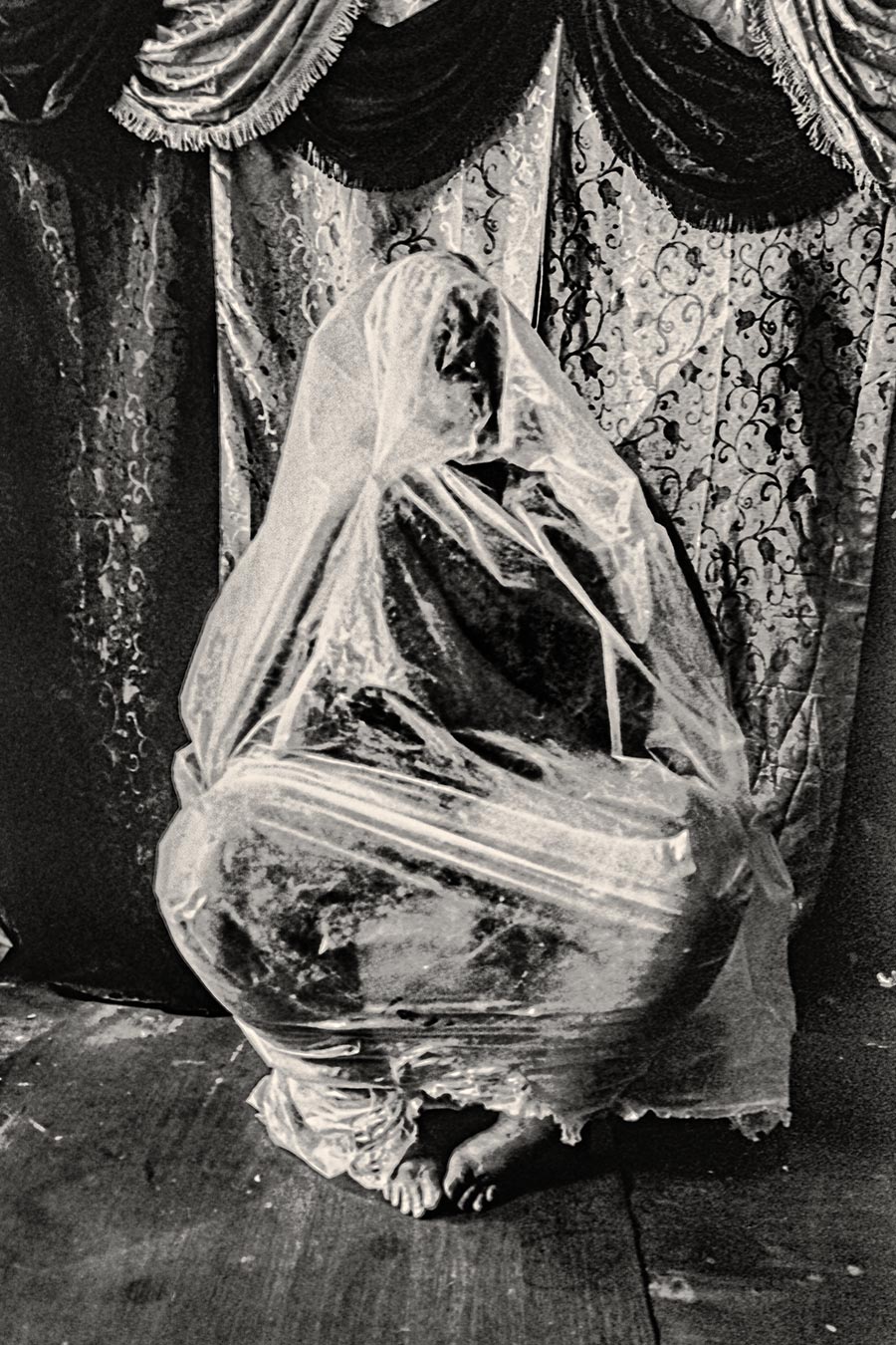 Schwarzweißfotografie eines in transparente Folie gehüllten menschlichen Körpers, nur die Zehen ragen heraus, analoges Körnungsbild