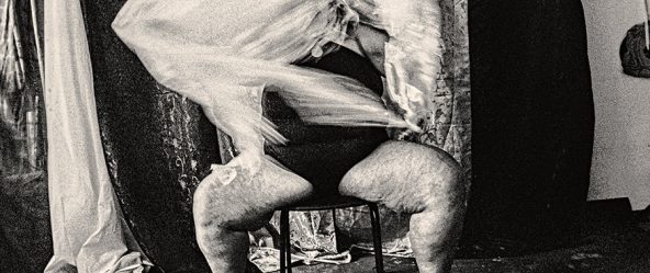 Bewegungsunschärfe von weißem Tüll über den Beinen einer sitzenden Person, analoges Schwarzweißfoto mit starkem Filmkorn