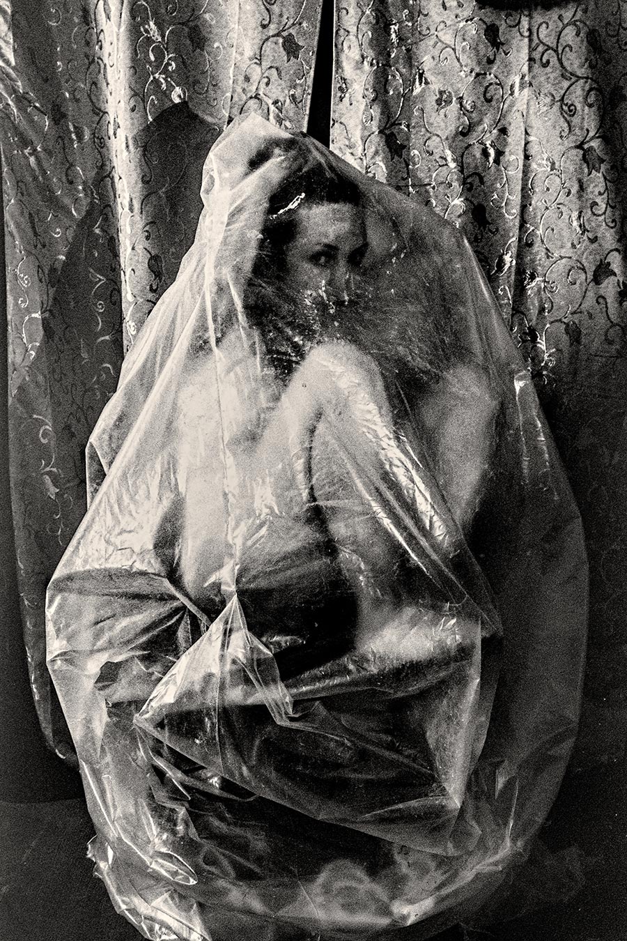 Frau vollständig in transparente Folie eingehüllt als Kokon, Blick durch das Material, analoges Schwarzweißfoto Fomapan Ortho 400