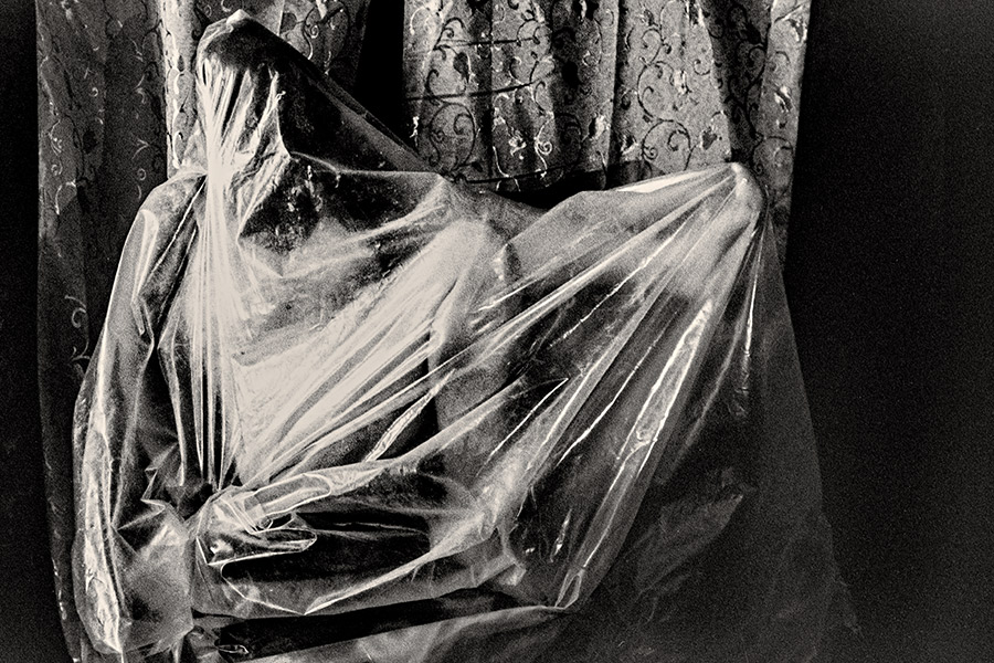 Von der Seite fotografierter in Folie gehüllter Körper, fast formlos, an gemustertem Vorhang, analoges Schwarzweißfoto Membran. Ich.