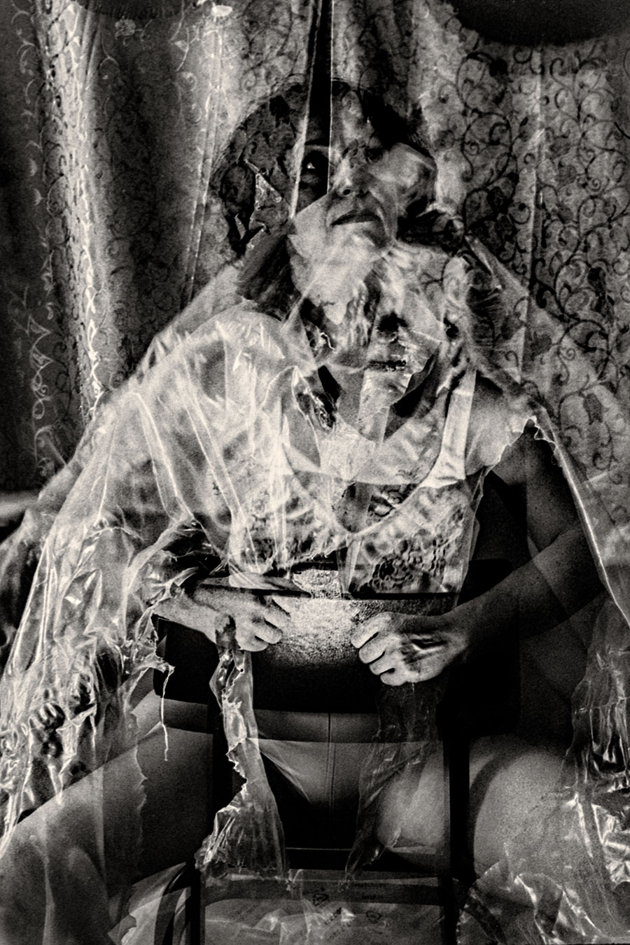 Sitzende Person mit zerrissener transparenter Folie über dem Körper, Blick durch Folienreste, analoges Schwarzweißfoto Fomapan Ortho 400-Doppelbelichtung