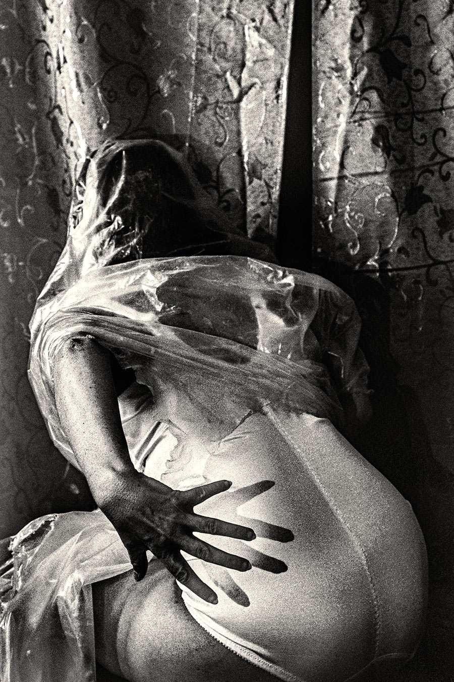 Rückenansicht einer in Folie gehüllten Person, Hand greift durch die Folie an die eigene Hüfte, analoges Schwarzweißfoto