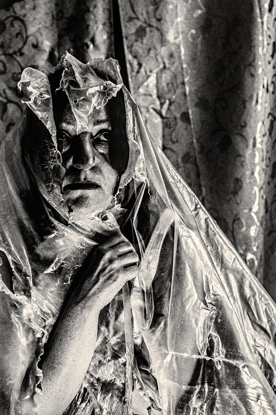 Nahaufnahme Gesicht mit zerrissener Folie die wie eine Maske wirkt, harter direkter Blick, analoges Schwarzweißfoto Fomapan Ortho 400 gepusht
