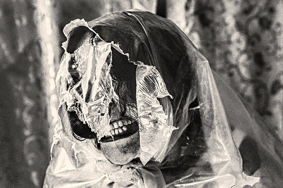 Nahaufnahme Gesicht mit zerrissener Folie in Fetzen, Mund geöffnet, Zähne sichtbar, dramatisches analoges Schwarzweißfoto Fomapan Ortho 400 gepusht