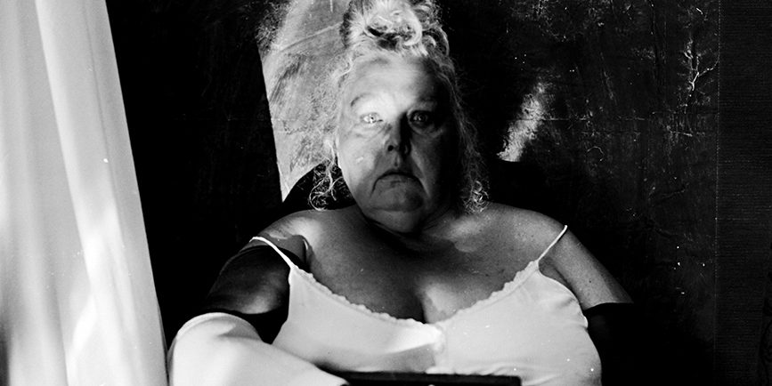 Analoges Selbstporträt Scala 200 Diafilm, frontales Portrait sitzender Frau mit starrem Blick, Rechenschieber vor dem Körper gehalten, schwarze Armstulpen, weiße Unterwäsche, Mamiya 645