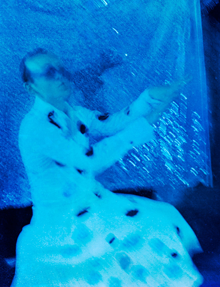 Verschwommene blaue Unterwasseraufnahme, Person mit ausgestreckten Armen in fließendem Stoff, monochrome Blaustimmung, analoge Langzeitbelichtung Meeresschnee 3