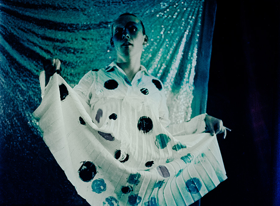 Frontalporträt mit ausgebreitetem gepunktetem Stoff, Person hält Kleid seitlich auf, türkiser Glitzerhintergrund, analoge Fotografie Meeresschnee 3, Mamiya645