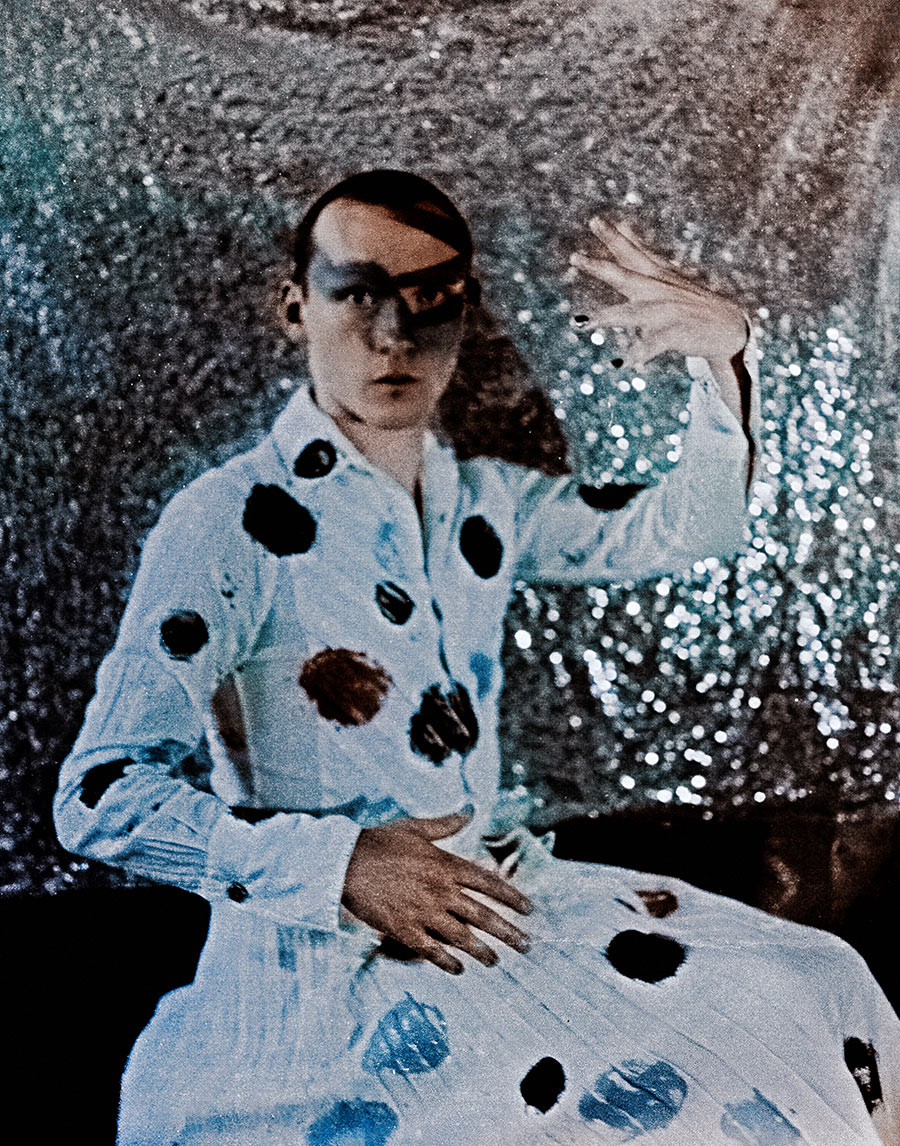 Sitzendes Porträt mit erhobener Hand, blaues Augen-Make-up, weißes geflecktes Gewand, silberner Glitzerhintergrund, analoge Mittelformatfotografie Meeresschnee 3, Mamiya645