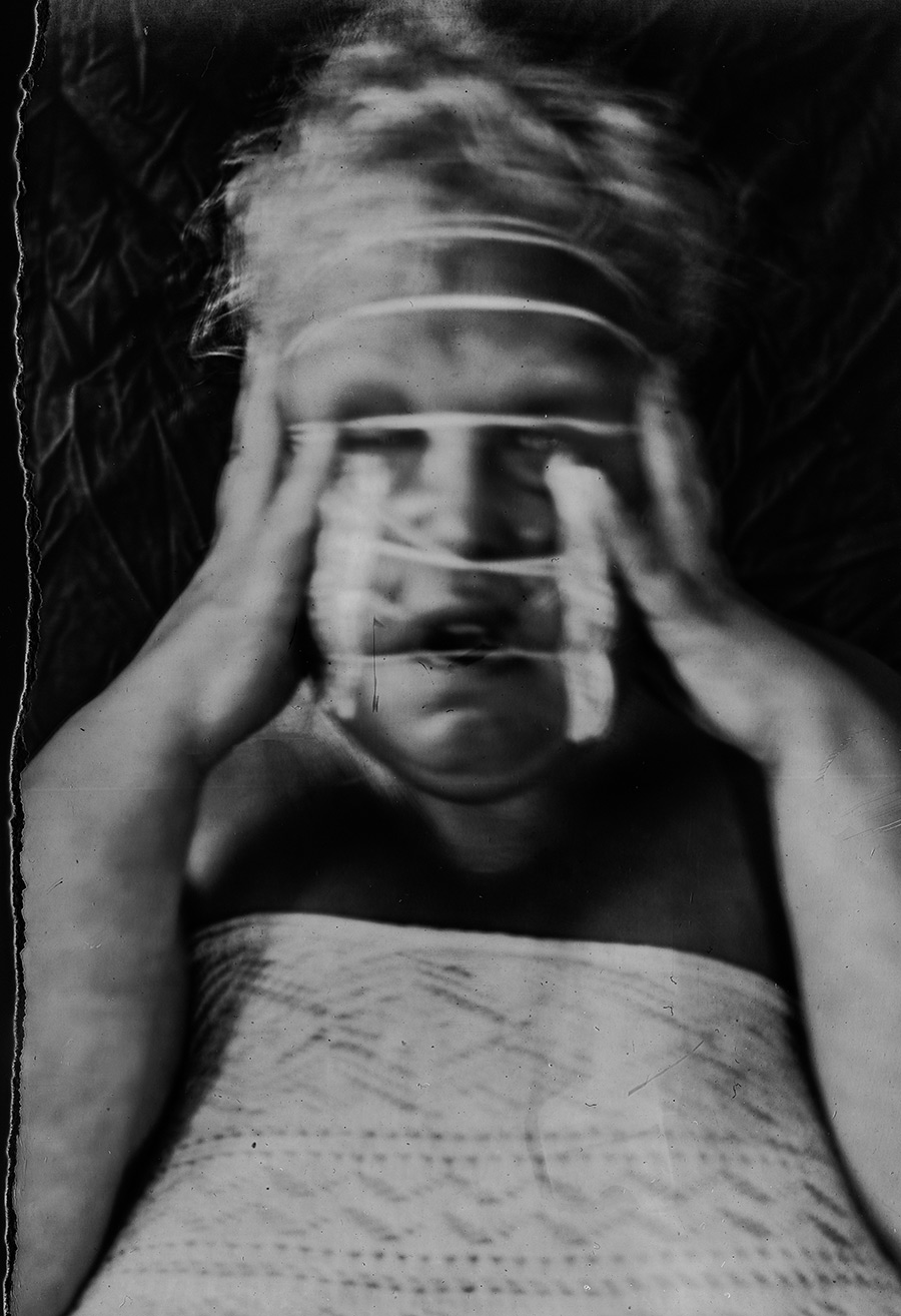 Analoges Selbstporträt auf Fotopapier, liegend, Hände an Schläfen gepresst, Gummibänder über Gesicht, starke Bewegungsunschärfe durch Langzeitbelichtung, Kamera Mentor, Serie Scheinbarkeit, Antje Kröger