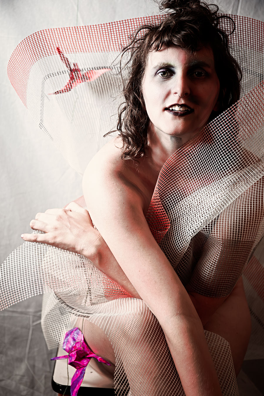 Porträt mit rot-weißem Netzstoff über Schulter und Arm, Blick direkt in Kamera, Bodypaint, pinker Origami-Kranich, Canon 6D, Aktfotokunst Vogelfrei