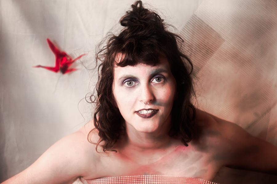 Frontalporträt mit hochgestecktem Haar, direkter Blick, Bodypaint in Rosa und Grau, roter Origami-Kranich, Netzstoff über Brust, Canon 6D, Vogelfrei Fotoserie