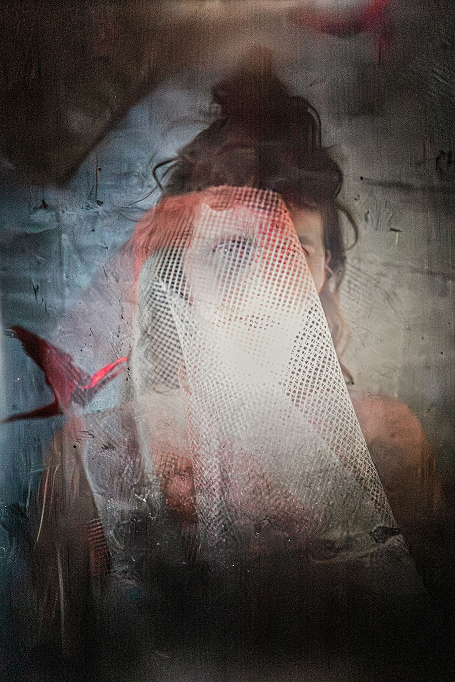 Verhülltes Gesicht hinter Netzstoff mit rotem Lichtschein, roter Origami-Kranich seitlich, Leica Q through the viewfinder Mentor, traumartige Fotografie Vogelfrei