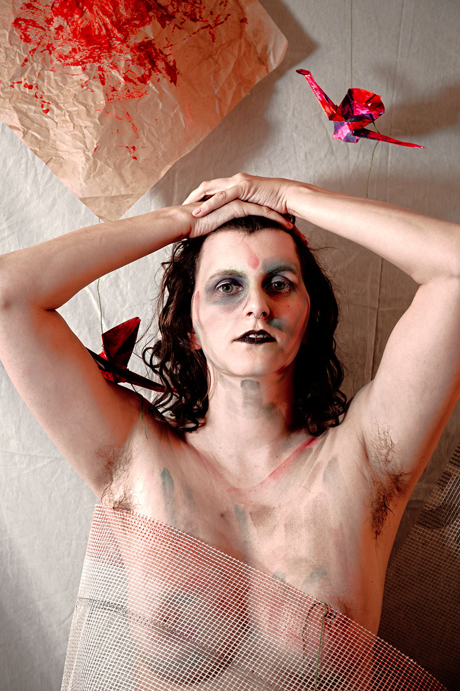 Aktporträt mit erhobenen Armen über dem Kopf, Bodypaint in Grau und Rot, Origami-Kranich im Hintergrund, Netzstoff über Oberkörper, Canon 6D, konzeptuelle Fotografie Vogelfrei