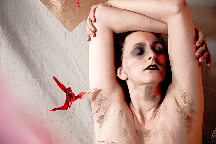 Aufsicht-Porträt mit verschränkten Armen über dem Gesicht, geschlossene Augen, roter Origami-Kranich, Bodypaint, Canon 6D, inszenierte Aktfotografie Vogelfrei
