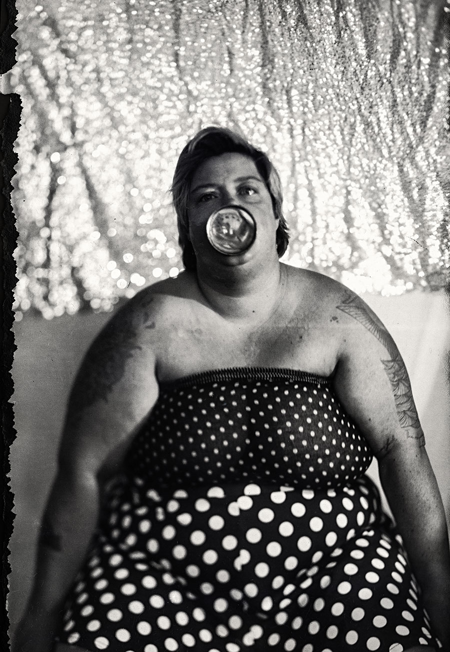 Frau hält geschmolzenes Thermometer aus Räucherofen an den Mund, gepunktetes Tuch, glitzernder Hintergrund, analoges Porträt mit Kamera Mentor auf Fotopapier, clowneske Fotoserie