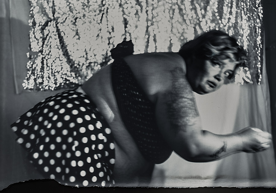 Bewegungsunscharfe Aufnahme einer dicken Frau im Ausfallschritt, gepunkteter Rock, glitzernder Hintergrund, analoge Großformatfotografie, clowneske Dynamik