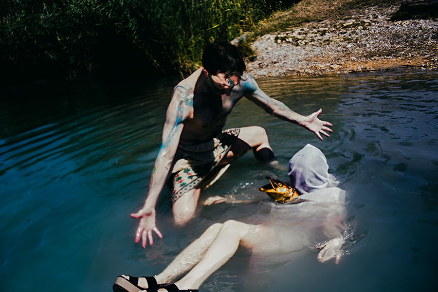 mann kniet über liegender figur im flachen wasser, fischmaske sichtbar, staged fotokunst fischtanz-serie, pentacon-objektiv