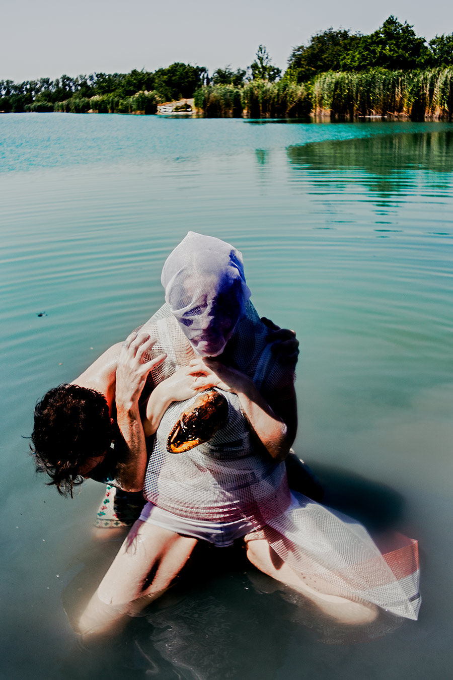 umarmung zweier bemalter figuren im see, eine mit weißer netzhaube und fischkopf am körper, staged fotokunst wasserperformance, fischtanz-serie, canon 6d