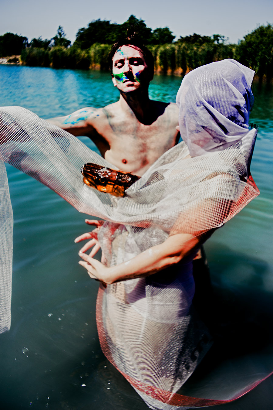 mann mit blau-grüner gesichtsbemalung hält netzstoff im wasser, tüllfigur im hintergrund, inszenierte analoge fotografie fischtanz, pentacon m42 objektiv
