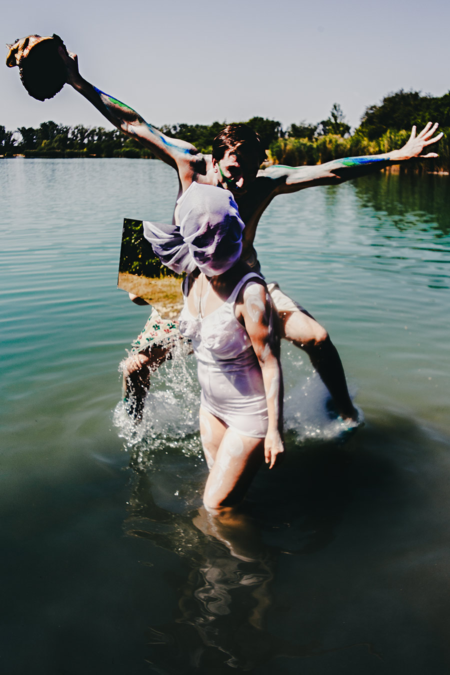 figur springt jubelnd aus dem wasser (balettsprung) mit fischkopf in erhobener hand, zweite person in weißer unterwäsche im vordergrund, fotokunst fischtanz-serie