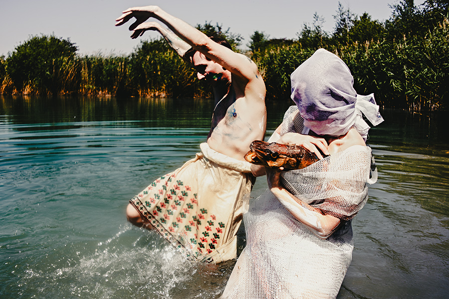 inszenierte fotokunst am see – mann mit bodypainting wirft arm nach oben, zweite figur mit weißer tüllhaube hält hecht im arm, fotoserie fischtanz, canon 6d mit pentacon-objektiv m42