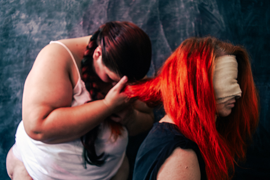 Dicke Frau berührt sanft die roten Haare einer Frau mit verbundenen Augen, Nahaufnahme der Hände im Haar, dunkler strukturierter Hintergrund, konzeptuelle Imagination-Fotoserie