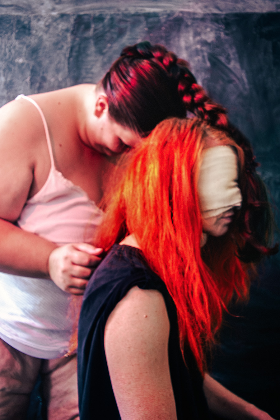 Zwei Frauen von hinten, dicker Körper im Rückenlicht, rote lange Haare der zweiten Figur mit Augenbinde aus Stoff, dunkler strukturierter Hintergrund, inszenierte Körperfotografie, analoge Optik