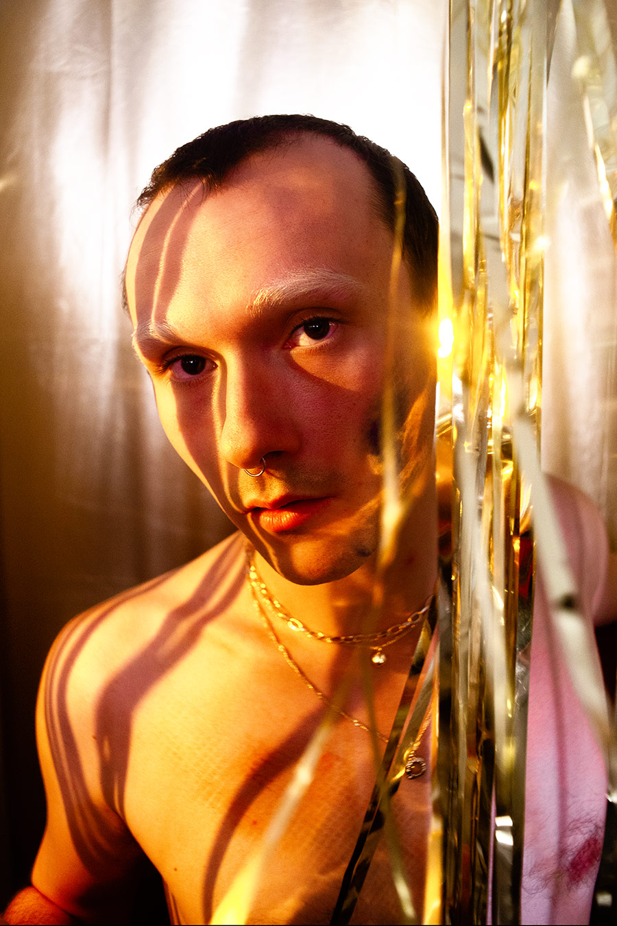 Porträt im Halbschatten, Gesicht zur Hälfte beleuchtet, Septum-Ring, Kettenschmuck, rosafarbener Stoff im Hintergrund, analog-digitale Aufnahmetechnik, konzeptuelle Selbstporträtserie Rausch