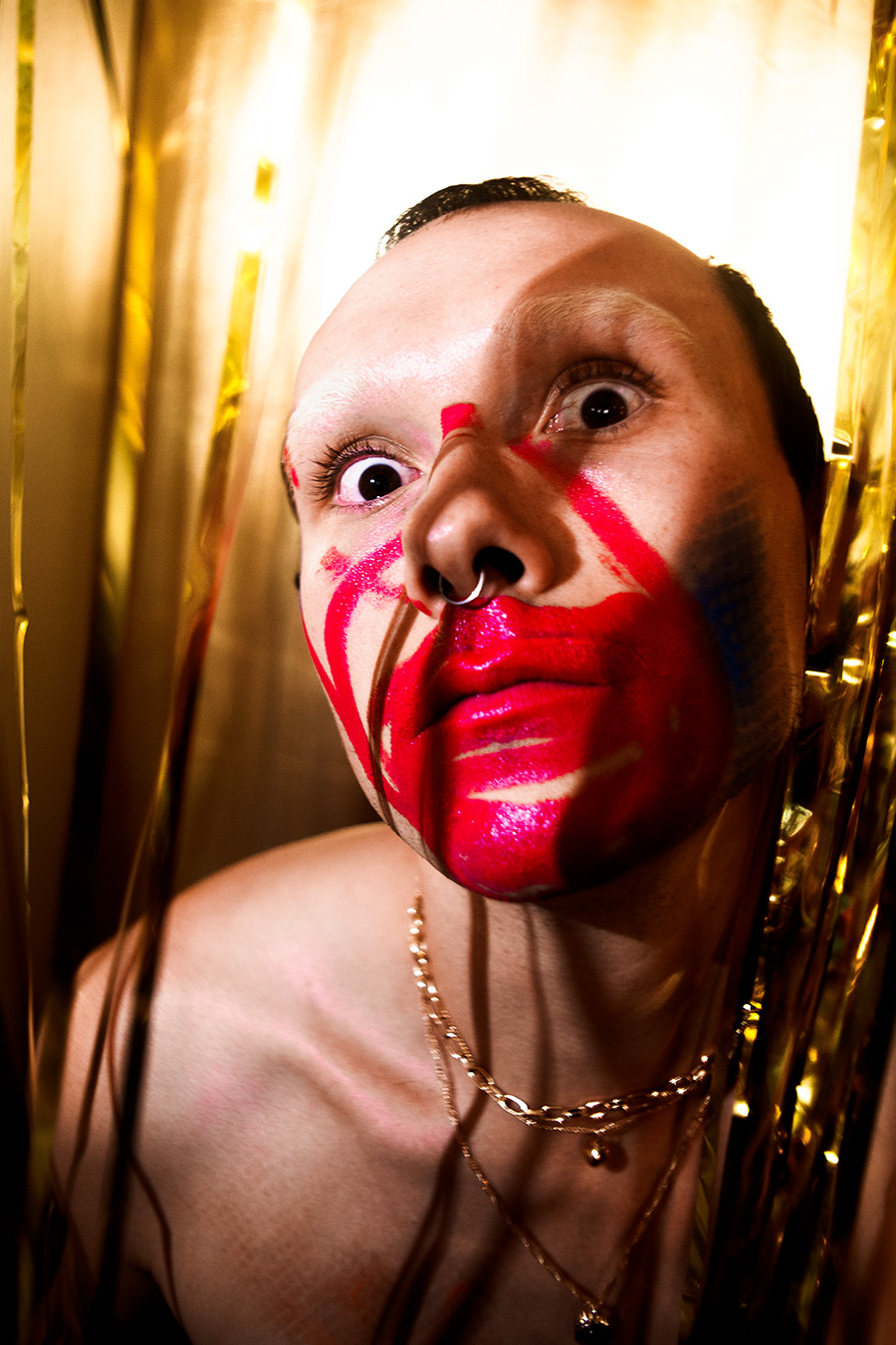 Weitwinkel-Nahaufnahme mit geweiteten Augen, rot-pinke Bemalung um den Mund, Septum-Ring, verzerrte Perspektive, Kettenschmuck, expressive Rauschzustand-Inszenierung, analog-digitale Fototechnik