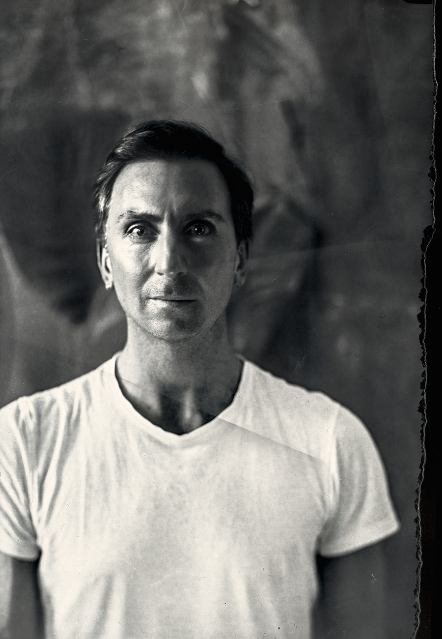 frontales porträt mann mit weißem t-shirt vor strukturiertem hintergrund, analog belichtetes agfapapier, fotoserie sprezzatura, kamera mentor