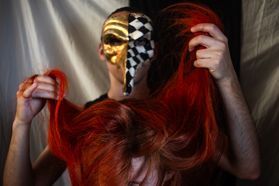 Person mit goldener Pestarztmaske im Hintergrund, zwei Hände heben rotes Haar seitlich empor, ruhige Bildkomposition, inszenierte Tod-Fotografie, analog-digitale Aufnahmetechnik
