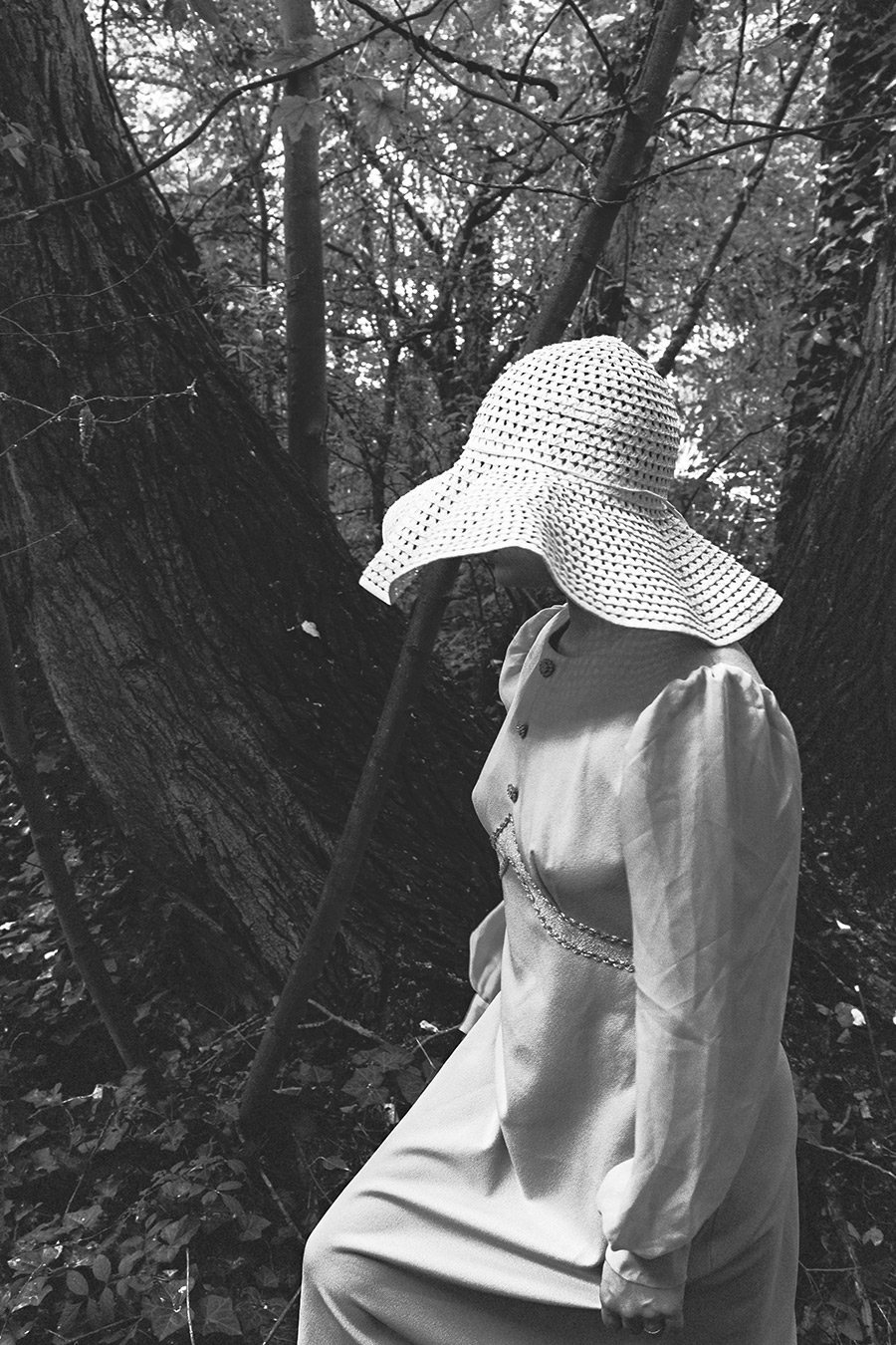 Schwarz-Weiß-Waldporträt einer argentinischen Tänzerin im Profil, weißer Häkelhut verdeckt das Gesicht, langes Vintage-Kleid, Bäume im Hintergrund, konzeptuelle Fotokunst