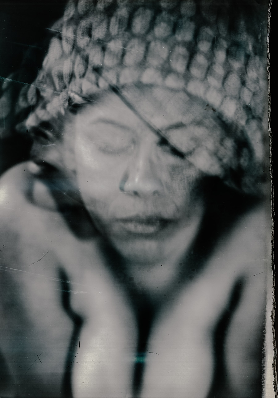 Unscharfes analoges Nahporträt mit netzartiger Kopfbedeckung über den Augen, Hände unter dem Kinn, Fotopapier-Großformatfotografie, konzeptuelle Arbeit über Erschöpfung
