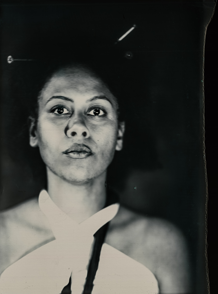 Analoges Frontalporträt mit wachem, direktem Blick, weißes Kleidungsstück am Hals, dunkler Hintergrund, Fotopapier-Großformatfotografie, konzeptuelle Serie über Stärke