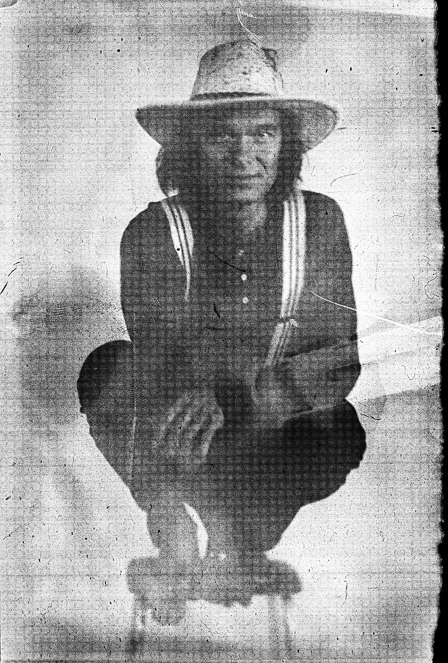 Person in Strohhut hockt mit gekreuzten Armen, gestreifte Hosenträger, körniges Schwarz-Weiß-Porträt auf Papiernegativ, analoge Großformatfotografie, Fotoserie Wolfsstunde
