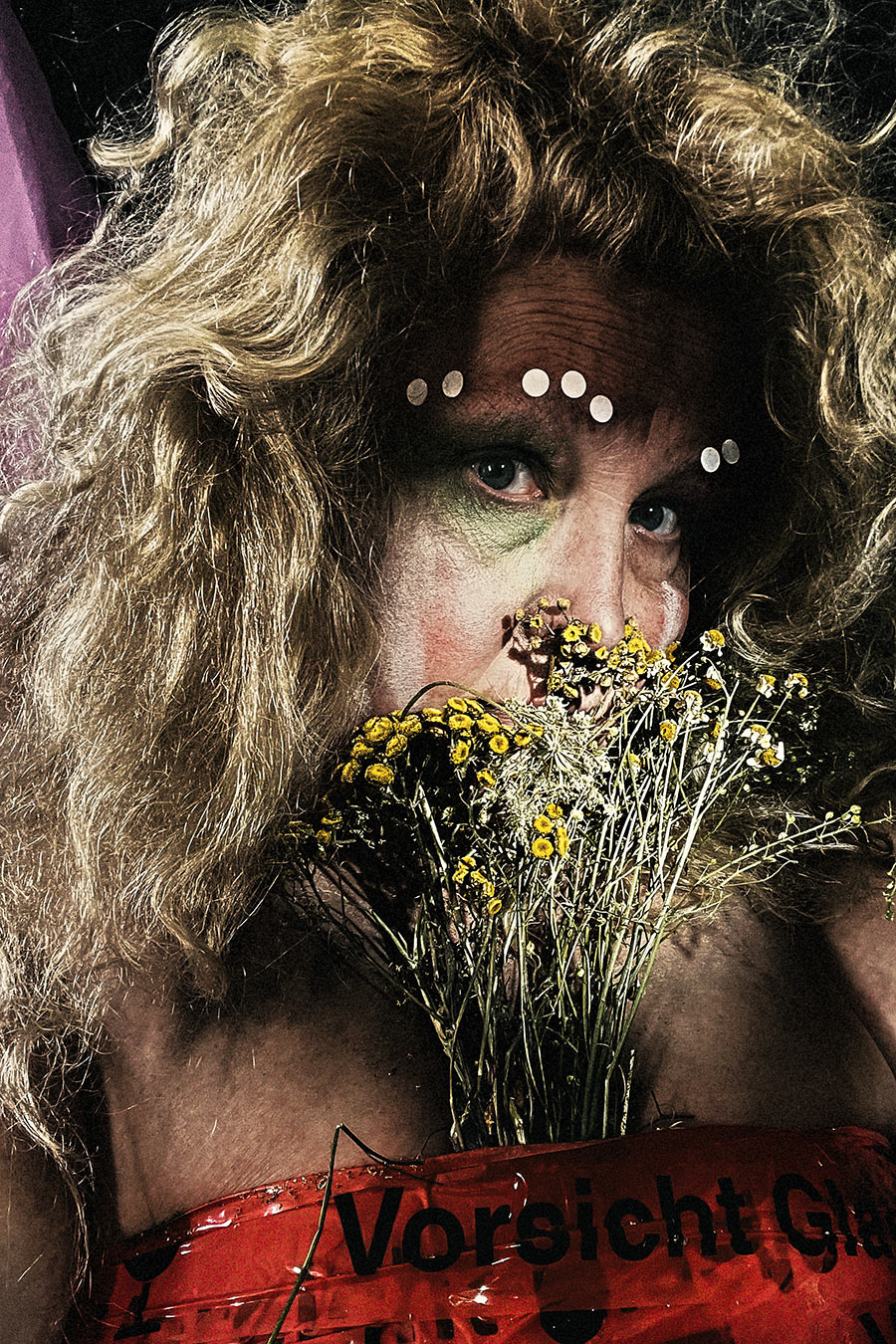 selbstporträt nahaufnahme, gelbe getrocknete blumen vor mund, wildes blondes haar, warnfolie vorsicht glas, konzeptuelle fotografie