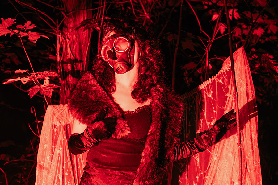 inszenierte Fotografie in rotem Kunstlicht, Figur mit Gasmaske und dunklen Locken, Pelzstola, Samthandschuhe, Spitzenvorhang zwischen Bäumen, Serie Потёмки